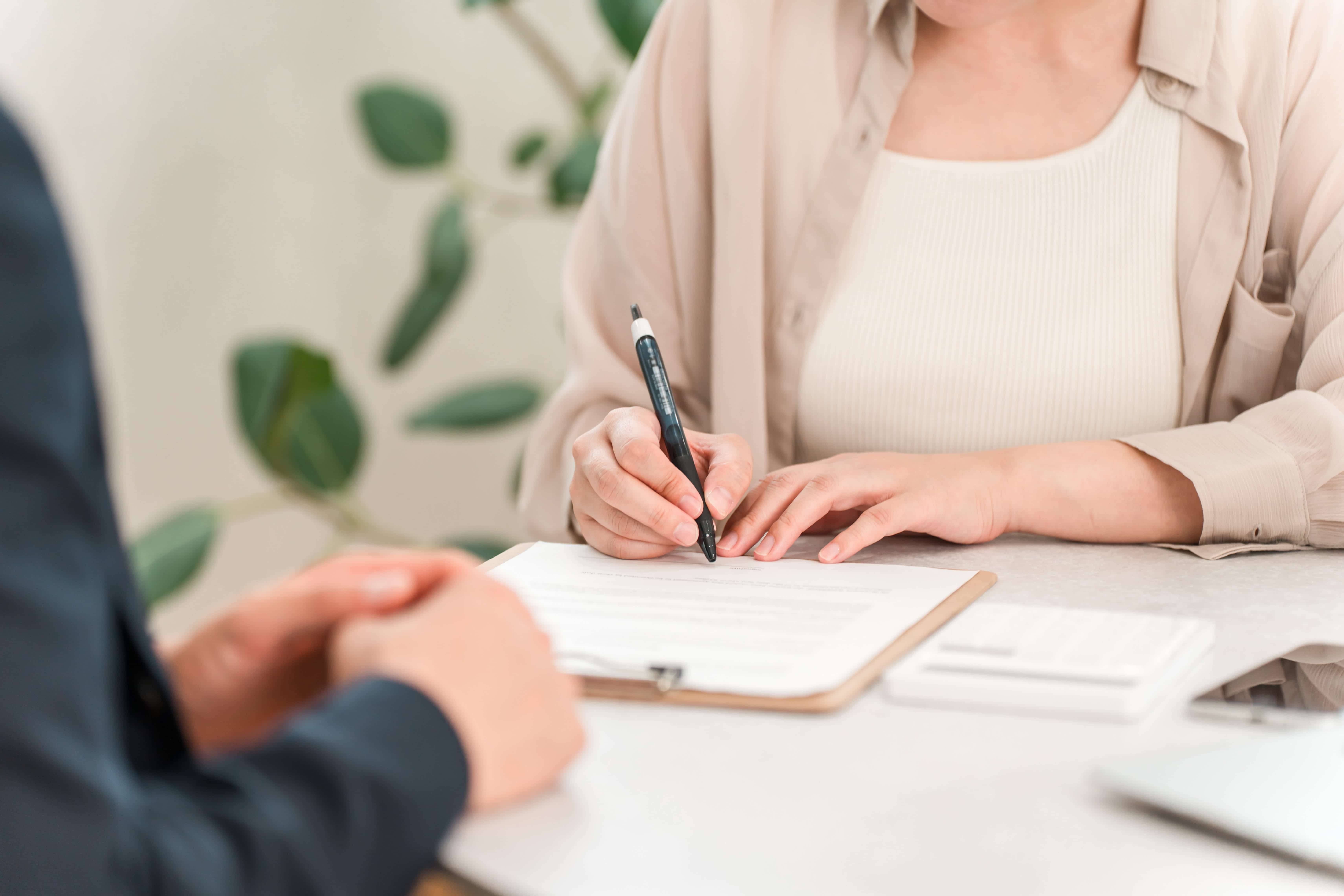 女性が担当者と向かい合いながら書類に記入しているシーン