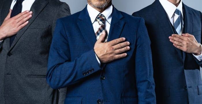 スーツ姿の3名のビジネスマンが胸に手を当て誠実さを示すポーズ