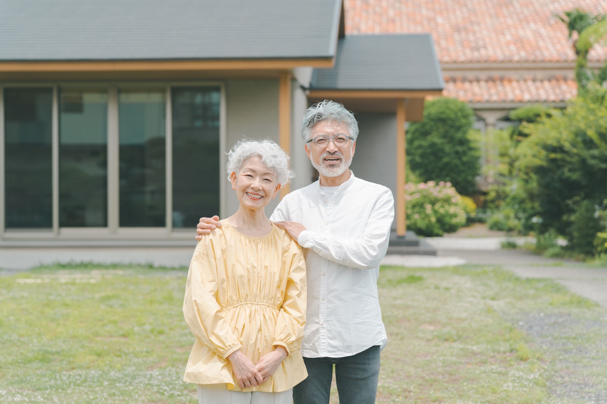 庭のある広い住まいの前に立つシニア夫婦